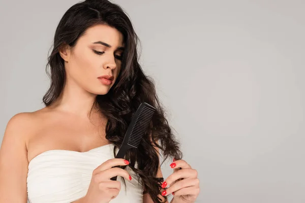 Brunette woman in white top brushing tangled hair with comb isolated on grey - foto de stock