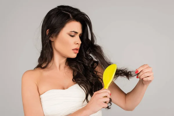 Upset woman in white top brushing long and tousled hair isolated on grey — Stock Photo