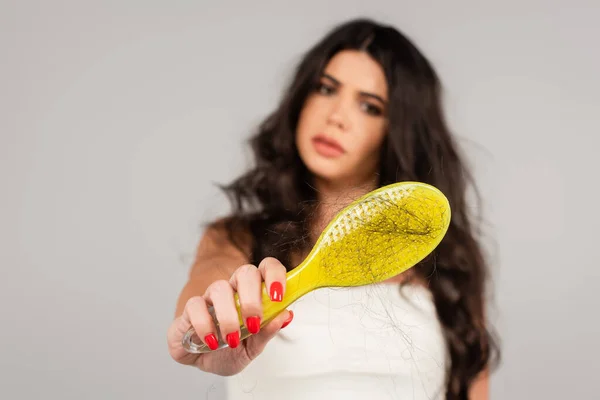 Upset woman showing hair brush with lost hair on blurred background isolated on grey — Stock Photo