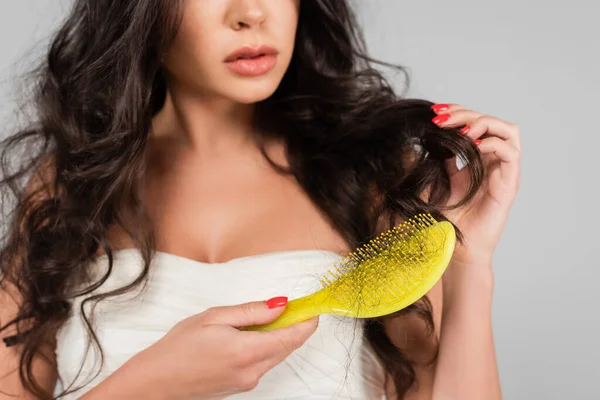 Partial view of brunette woman brushing damaged hair isolated on grey — Stock Photo