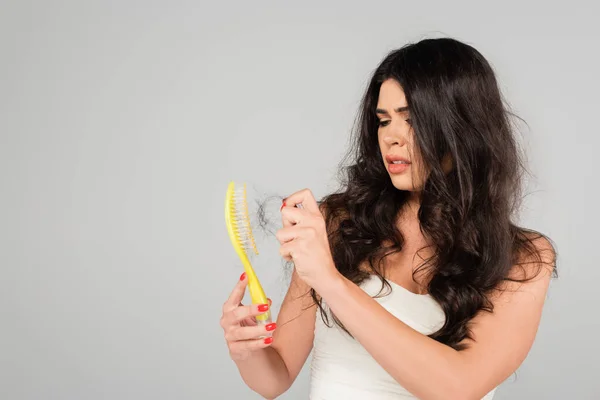 Brunette woman with hair loss problem cleaning hair brush isolated on grey — Stock Photo