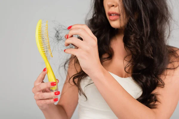 Partial view of brunette woman with hair loss problem cleaning hair brush isolated on grey — Stock Photo