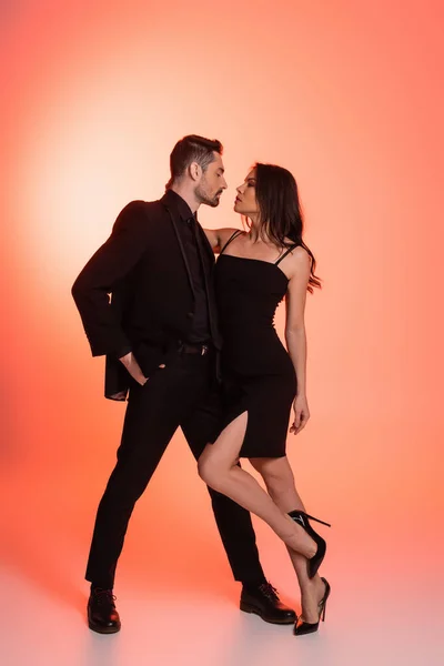 Full length of sexy man in black formal wear standing with hand in pocket and seducing woman on pink — Stock Photo