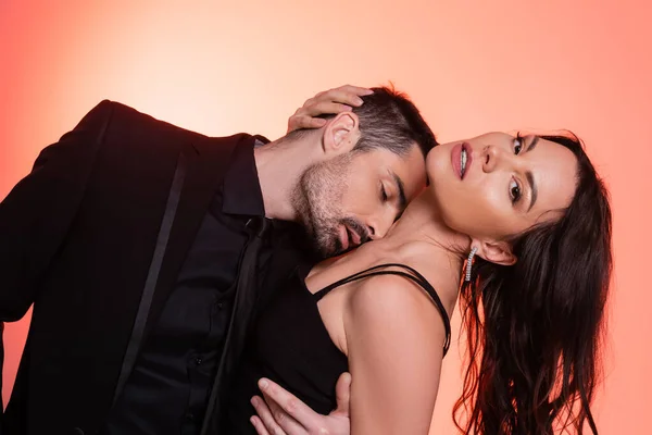 Passionate and bearded man in suit kissing chest of sexy woman on pink — Photo de stock