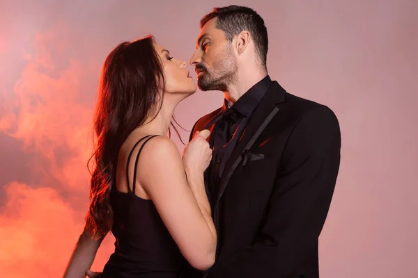 Sexy woman in black dress pulling tie while seducing man in formal wear on pink and grey — Stock Photo