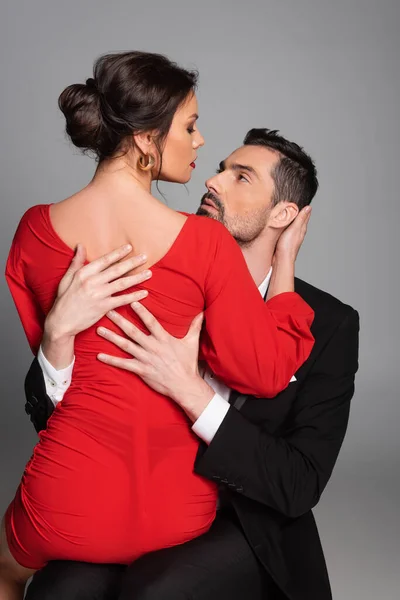 Passionate man hugging sexy girlfriend in red dress isolated on grey — Stock Photo