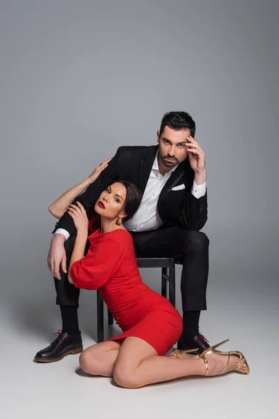 Sexy woman touching boyfriend while sitting on floor on grey background — Stock Photo