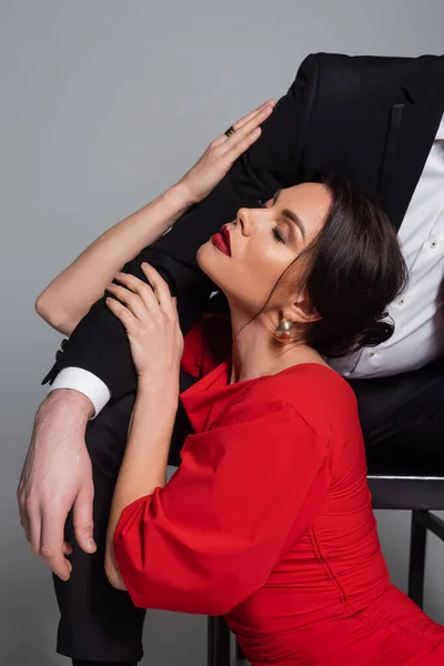 Sexy woman in red dress touching boyfriend in suit on grey background — Stock Photo