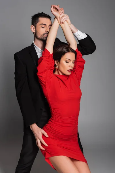 Bearded man touching hands and hip of sexy girlfriend in red dress isolated on grey — Stock Photo