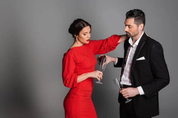 Elegant man in suit pouring champagne in glass of girlfriend in dress on grey background — Stock Photo