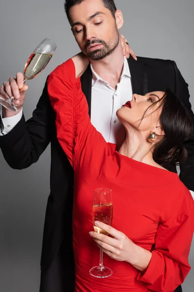 Seductive woman in red dress hugging boyfriend with champagne on grey background — Stock Photo