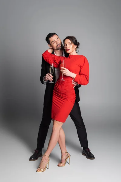Full length of elegant woman hugging boyfriend and holding champagne on grey background — Stock Photo