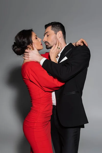 Side view of sexy woman in dress kissing elegant boyfriend on grey background — Stockfoto