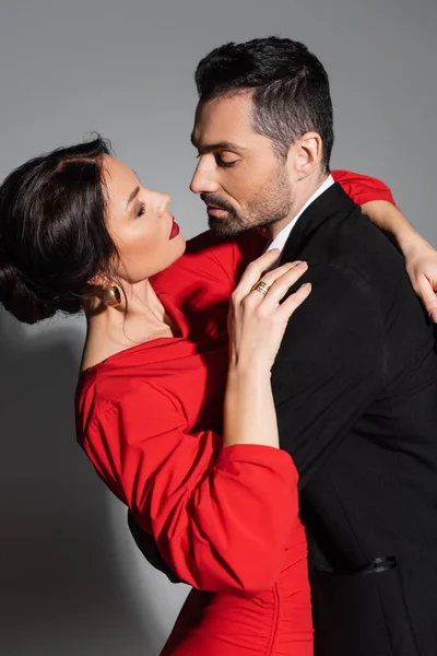 Sensual brunette woman hugging boyfriend in suit on grey background — Stock Photo
