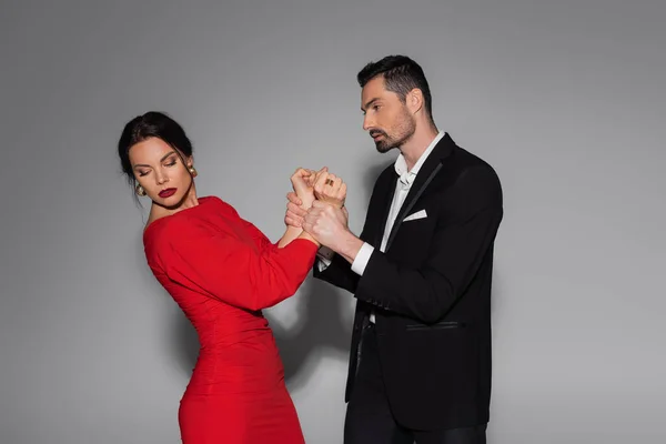 Elegant man holding hands of woman in red dress on grey background — Stock Photo