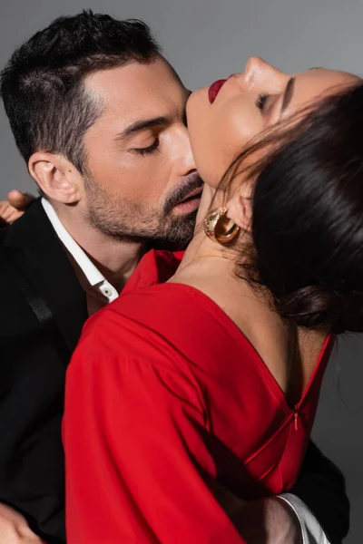 Elegant man in suit kissing neck of sensual girlfriend on grey background — Photo de stock