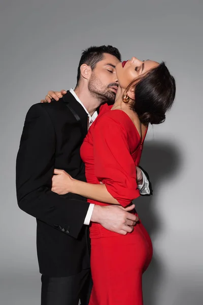 Sexy man in suit kissing elegant woman in dress on grey background — Stock Photo