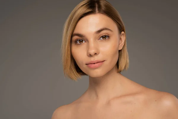 Blonde woman with brown eyes and naked shoulders looking at camera isolated on grey — Stock Photo