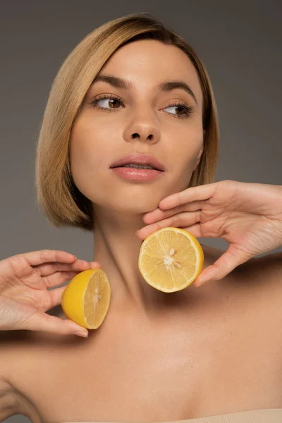 Young woman with bare shoulders holding lemon halves isolated on grey — Stock Photo