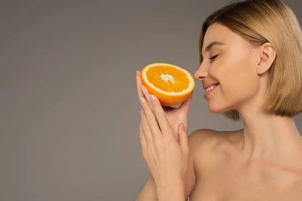 Side view of cheerful woman with closed eyes smelling orange isolated on grey — Stockfoto