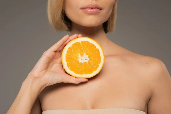 Cropped view of young woman with bare shoulders holding juicy orange isolated on grey - foto de stock