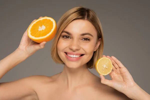 Cheerful young woman holding juicy orange and sour lemon isolated on grey — Fotografia de Stock