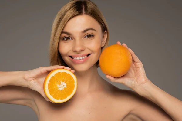 Cheerful blonde woman holding juicy oranges isolated on grey - foto de stock
