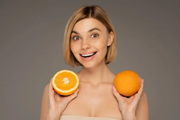 Amazed young woman holding ripe oranges isolated on grey — Stockfoto