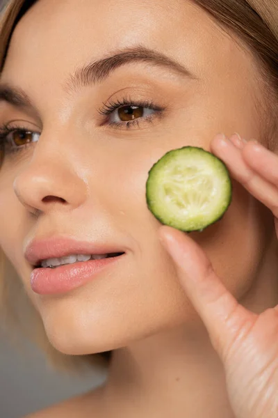 Close up of young woman holding sliced and fresh cucumber near cheek - foto de stock