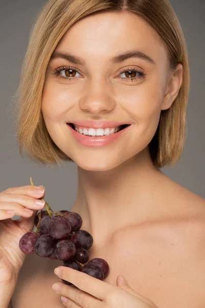Happy young woman holding fresh grapes and smiling isolated on grey — Fotografia de Stock