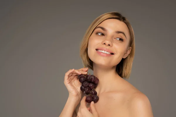 Cheerful young woman holding fresh grapes and smiling isolated on grey — Fotografia de Stock