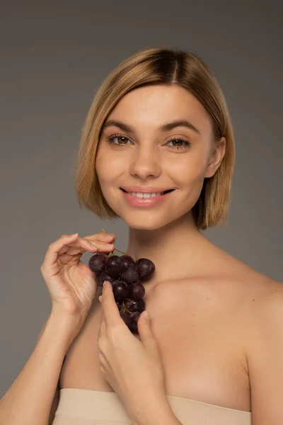 Smiling young woman holding fresh grapes and smiling isolated on grey — Fotografia de Stock