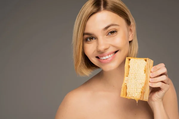 Cheerful young woman with bare shoulders holding honeycomb isolated on grey — Foto stock