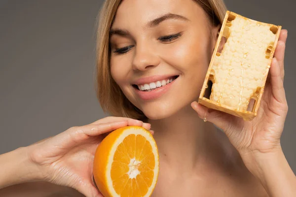 Happy young woman holding honeycomb and orange isolated on grey — Stock Photo