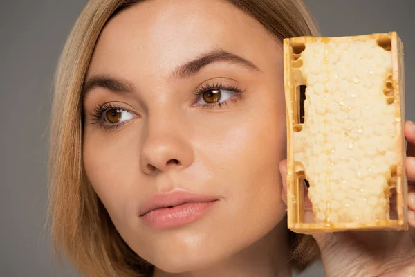 Close up of young woman holding sweet honey in honeycomb isolated on grey — Stock Photo