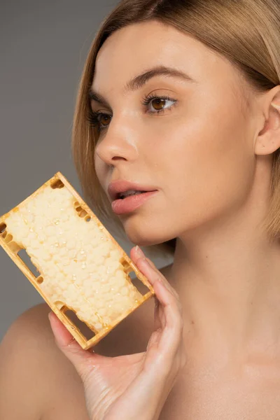 Close up of young woman with bare shoulder holding sweet honey in honeycomb isolated on grey — Foto stock