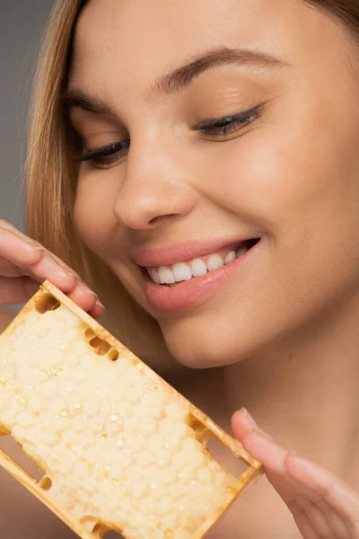Close up of happy woman holding sweet honey in honeycomb isolated on grey — Foto stock