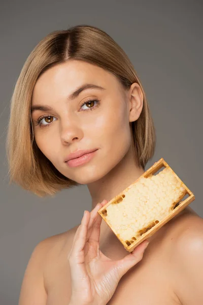 Blonde young woman holding wooden frame with sweet honey isolated on grey — Stockfoto