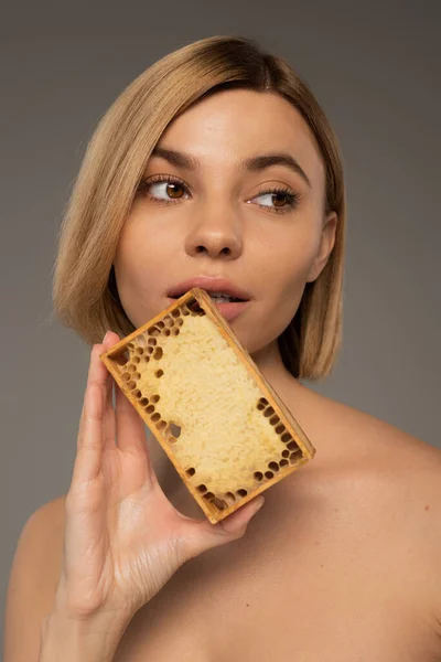 Блондинка молода жінка тримає дерев'яну раму з солодким медом біля обличчя ізольовано на сірому — стокове фото