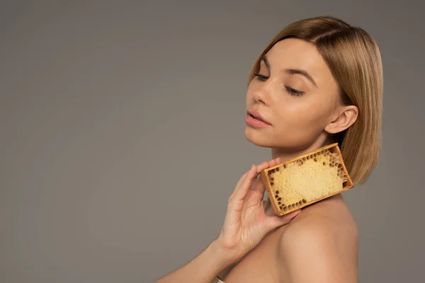 Blonde young woman holding wooden frame with sweet honey near neck isolated on grey — Foto stock