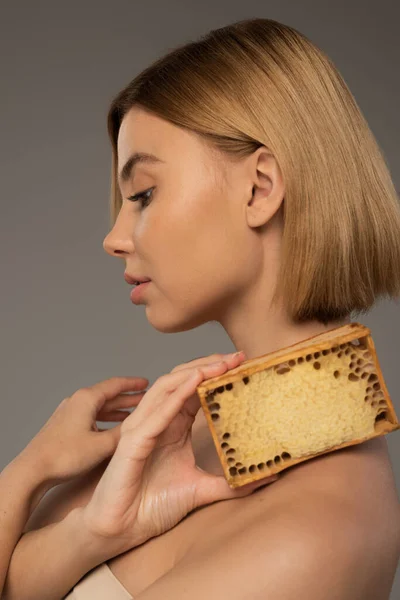 Side view of blonde woman holding honeycomb in wooden frame isolated on grey — Fotografia de Stock