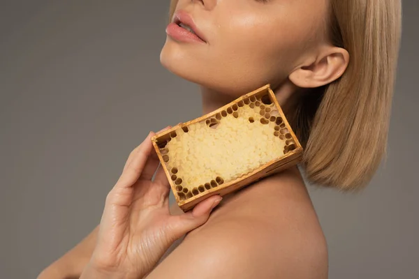 Обрізаний вид на блондинку молоду жінку, що тримає дерев'яну раму з солодким медом ізольовано на сірому — стокове фото