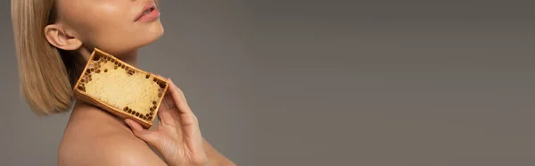 Cropped view of blonde young woman holding wooden frame with sweet honey isolated on grey, banner — Fotografia de Stock