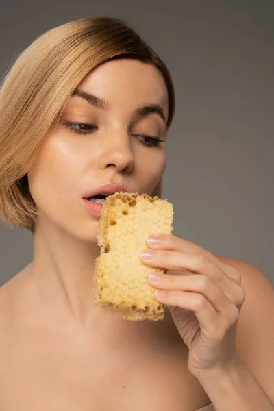 Young woman holding piece of sweet honeycomb near mouth isolated on grey — Stock Photo