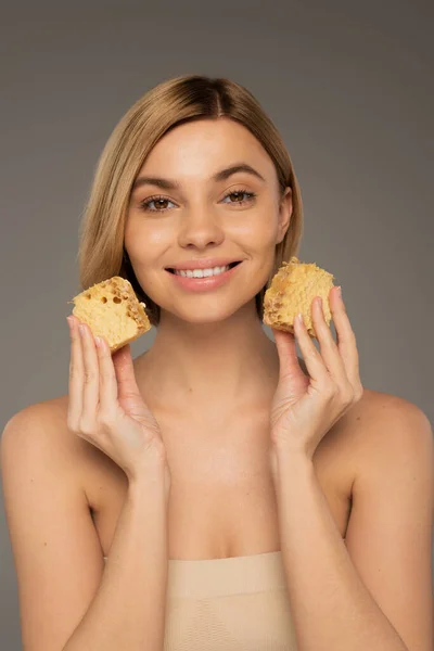 Pleased young woman holding sweet honeycombs isolated on grey — Stock Photo