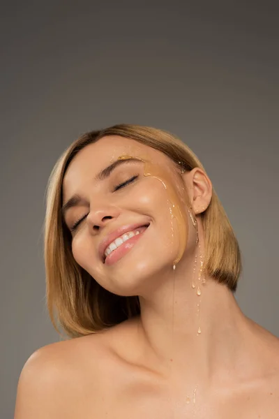Щаслива молода жінка з солодким медом на щоці посміхається ізольовано на сірому — стокове фото