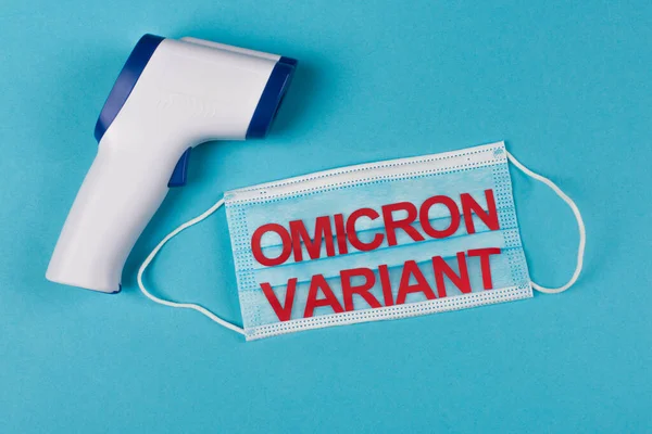 Top view of non-contact pyrometer near medical mask with omicron variant lettering on blue background — Photo de stock