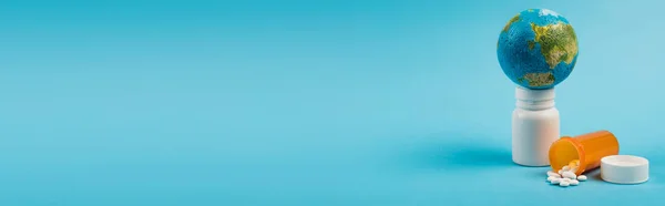 Маленький глобус на банку с таблетками от нового штамма omicron на голубом фоне с копировальным пространством, баннер — стоковое фото