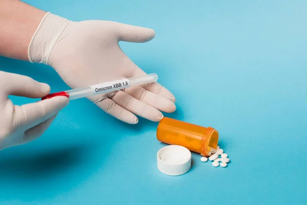 Cropped view of doctor in latex gloves holding throat swab with omicron lettering near pills on blue background — Photo de stock