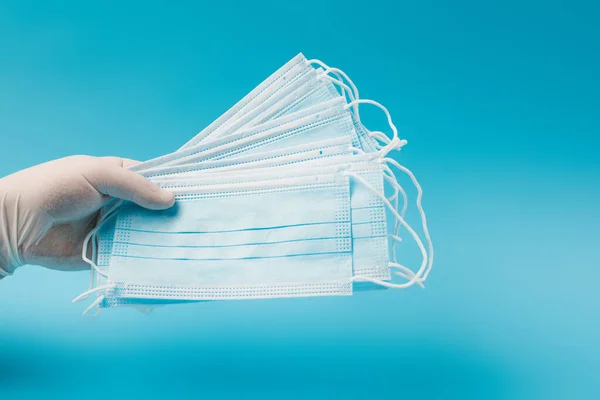 Cropped view of doctor in latex gloves holding medical masks isolated on blue - foto de stock